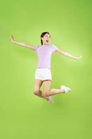 full kropp ung asiatisk tjej som hoppar, isolerad på grön bakgrund foto