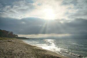 solnedgång på de väst strand på de baltic hav. vågor, strand, molnig himmel och solsken foto