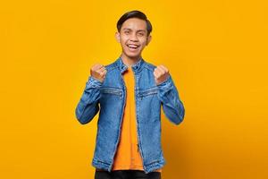 porträtt av upphetsad ung asiatisk man som firar framgång med upphöjda händer isolerad på gul bakgrund foto