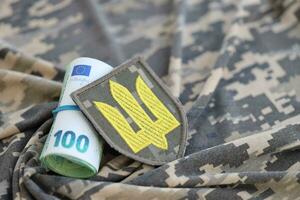 ukrainska armén symbol och knippa av euro räkningar på militär enhetlig. betalningar till soldater av de ukrainska armén från europeisk union, löner till de militär. krig Stöd foto