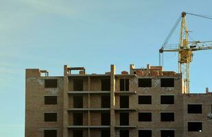 se av en stor konstruktion webbplats med byggnader under konstruktion och flera våningar bostads- hem. torn kranar i verkan på blå himmel bakgrund. hus renovering begrepp foto