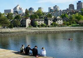 människor njuter en solig vår dag nära de vatten i de parkera, med en fantastisk stadsbild i de bakgrund. vancouver, före Kristus, Kanada. Maj 02, 2021. foto