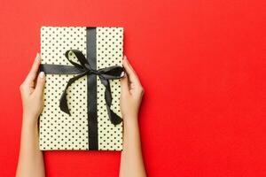 kvinnliga händer innehav randig gåva låda med färgad band på röd bakgrund. jul begrepp eller Övrig Semester handgjort närvarande låda, begrepp topp se med kopia Plats foto
