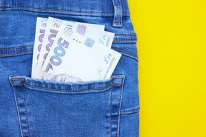platt lägga, detalj av denim jeans med ukrainska hryvnian räkningar i ficka på gul bakgrund. foto