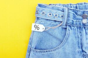 platt lägga, detalj av denim jeans och vit etiketter på gul bakgrund foto