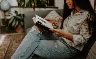 närbild skott av en sydasiatisk ung kvinna som sitter i soffan och läser en bok foto