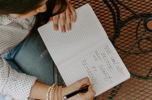 närbild skott av en sydasiatisk ung kvinna som skriver något i kopiboken som sitter i caféet