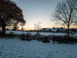 solnedgång i främre av engelsk lantlig landsbygden i vinter- med snö foto