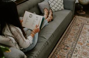 närbild skott av en sydasiatisk ung kvinna som sitter i soffan och läser en bok foto