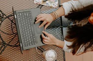 ovanifrån av en sydasiatisk ung kvinna som arbetar med datorn i caféet
