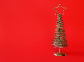 gyllene metall jul träd med en stjärna på topp, röd bakgrund. foto