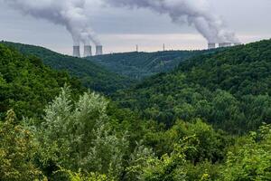 grön dal täckt med skog och på de horisont är de kyl- torn av en kärn kraft växt dukovany. kontrast av natur och industri. tjeck republik. foto