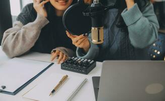 kvinna inspelning en podcast på henne bärbar dator dator med hörlurar och en mikroskop. kvinna podcaster framställning audio podcast från henne Hem studio. foto