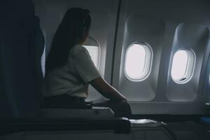 silhuett av kvinna utseende ut de fönster av ett flygande flygplan. passagerare på de plan vilar bredvid de fönster. foto
