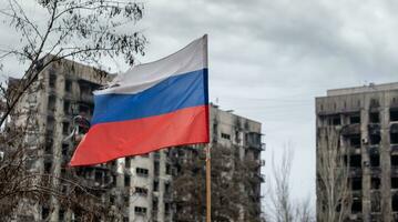 tricolor flagga av ryssland mot de bakgrund av förstörd och bränd hus i ukraina foto