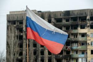 tricolor flagga av ryssland mot de bakgrund av förstörd och bränd hus i ukraina foto