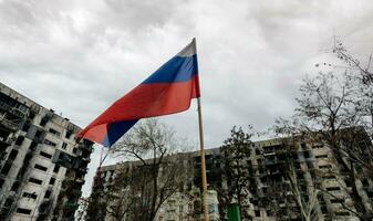 tricolor flagga av ryssland mot de bakgrund av förstörd och bränd hus i ukraina foto