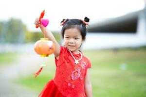 porträtt asiatisk unge flicka innehav teng lang lampa kinesisk stil. barn bär röd qipao cheongsam. kinesisk ny år begrepp. Lycklig barn fira årlig festival. foto