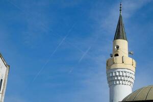 torn av de minaret av de moské mot de blå himmel och de contrail från flygplan. foto