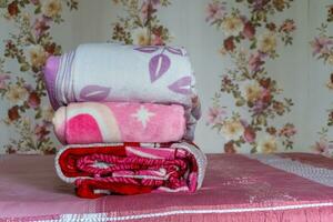staplade av färgrik filt på rosa säng. vikta rosa filtar. vit vikta täcke liggande foto
