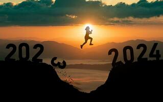silhuett kvinna hoppa Lycklig ny år 2024 begrepp, kvinnor som hoppar över barriär klippa och Framgång från 2023 klippa till 2024 klippa med solnedgång bakgrund. Lycklig ny år för webb baner och annons. foto