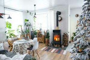 festlig vit modern interiör av hus är dekorerad för jul och ny år i loft stil med svart spis, öppen spis, jul träd. inlagd växter, ved i de vedtrave foto