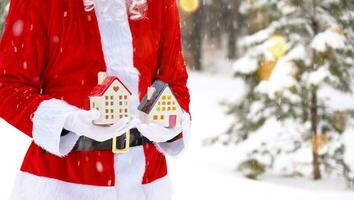 santa försiktigt innehar i hans händer en mycket liten hus i en små storlek i snö utomhus- - en gåva för jul, ny år, de uppfyllelse av en dröm. skydd, försäkring, inteckning, inköp av hus foto