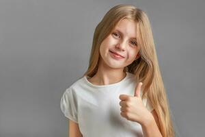 Lycklig barn, liten flicka som visar tummen upp gest i en vit t-shirt foto