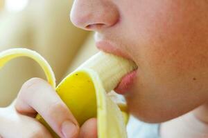 porträtt av en Tonårs pojke äter en banan. Foto av en killar mun och mun med en banan. färsk frukt. friska livsmedel för barn