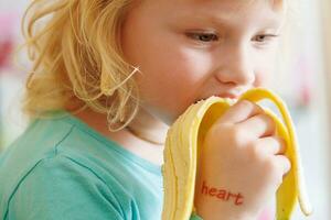 porträtt av en liten flicka äter en banan. de begrepp av friska mat. en färsk snabbt mellanmål foto