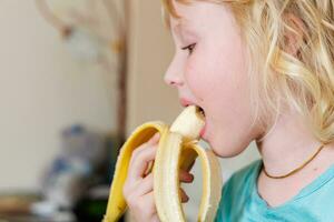 porträtt av en liten flicka äter en banan. de begrepp av friska mat. en färsk snabbt mellanmål foto