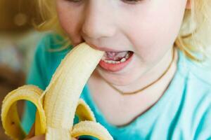 porträtt av en liten flicka äter en banan. de begrepp av friska mat. en färsk snabbt mellanmål foto