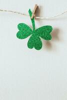 grön glitter shamrocks dekoration. skinande papper skära klöver blad på klädnypa. Lycklig st. patricks dag foto