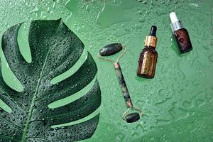 skönhet kosmetisk lotion serum flaska och jade massage vält. behandling hudvård begrepp med monstera blad och vatten droppar bakgrund foto