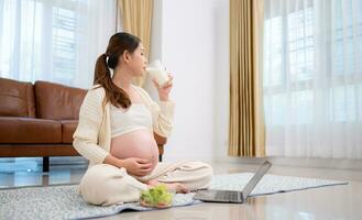 gravid kvinna dricka mjölk medan Sammanträde på de golv på Hem foto