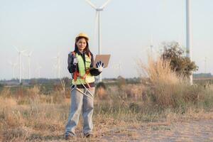 kvinna ingenjör bär säkerhet hjälm och innehav bärbar dator i vind turbin odla. foto