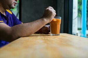 man drycker utsökt thai mjölk te medan Sammanträde på en tabell i en Kafé. foto