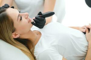 baner bearbeta kvinna applicering permanent tatuering smink på mun i kosmetolog salong foto