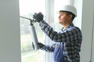 indisk arbetstagare använder sig av en silikon rör för reparation av fönster inomhus- foto