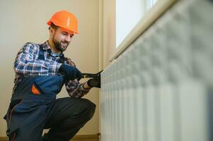 ung man rörmokare kontroll radiator medan montera uppvärmning systemet i lägenhet foto