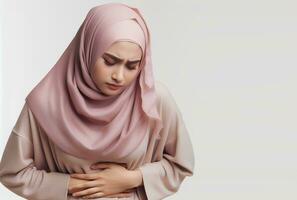 ai genererad asiatisk muslim kvinna i hijab med händer innehav mage med smärta ansiktsbehandling uttryck isolerat vit bakgrund foto