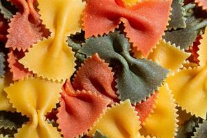 okokt vibrerande färgad farfalle pasta. en kulinariska duk av flerfärgad fluga makaroner, skapande en livlig och texturerad bakgrund för gourmet matlagning entusiaster. färgad torr pasta. rå makaroner foto