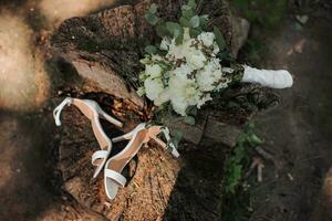 bröllop bukett på en träd. bröllop detaljer på en trä- stubbe i de parkera. en skön bukett av vit blommor. brudens skor foto