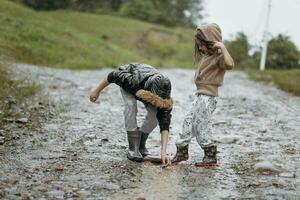 två Lycklig liten flickor av europeisk utseende spelar i vattenpölar under regn i sommar. barn är spelar i de regn. barn spelar i natur utomhus. de flicka åtnjuter de regn. foto