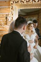 en skön brud i en bröllop klänning med en skön frisyr och en brudgum i en svart kostym i en skön trä- interiör försiktigt rörande varje Övrig. reflexion i de spegel foto