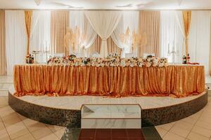 de bröllop tabell av de brud och brudgum, dekorerad med blommor, är tillverkad i grå Färg. ljus på står. blommor och grönska. guld. bröllop detaljer foto