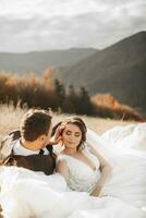 porträtt av en eleganta brudgum med en brud på en bakgrund av höst torr gräs. de begrepp av en lantlig bröllop i de berg, Lycklig bohemisk nygifta. de brud och brudgum är liggande på de gräs foto