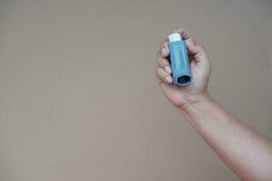 stänga upp kvinna hand håll astma inhalator, brun bakgrund. begrepp, hälsa vård. farmaceutisk Produkter för behandling symptom av astma eller copd. använda sig av under recept. hälsa vård enhet på Hem. foto