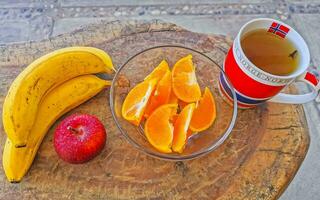 bananer skivad apelsiner och röd äpple frukt och ingefära te. foto