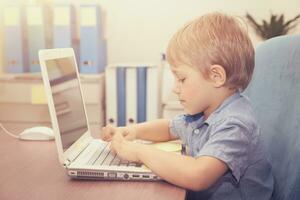 liten pojke arbetssätt på de bärbar dator foto